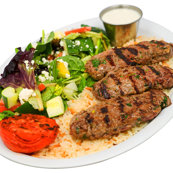 Three grilled kofta kebabs with rice, a fresh salad, grilled tomato, and white sauce.