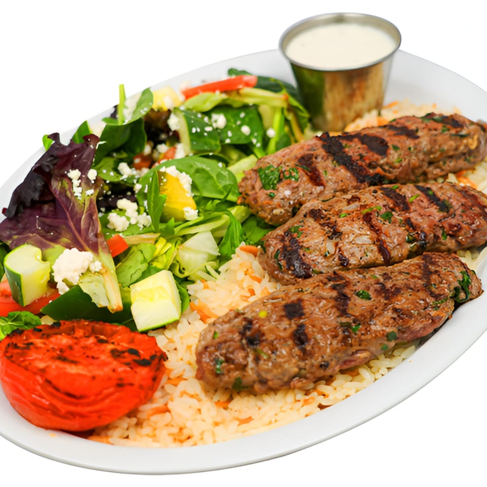 Three grilled kofta kebabs with rice, a fresh salad, grilled tomato, and white sauce.